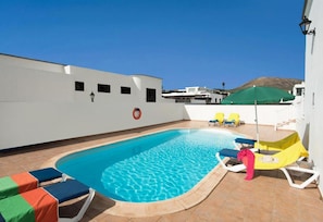 Una piscina en la azotea con sillas de descanso y una sombrilla verde.