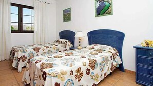 Quarto com duas camas, uma janela com cortinas, uma luminária e um penteado.