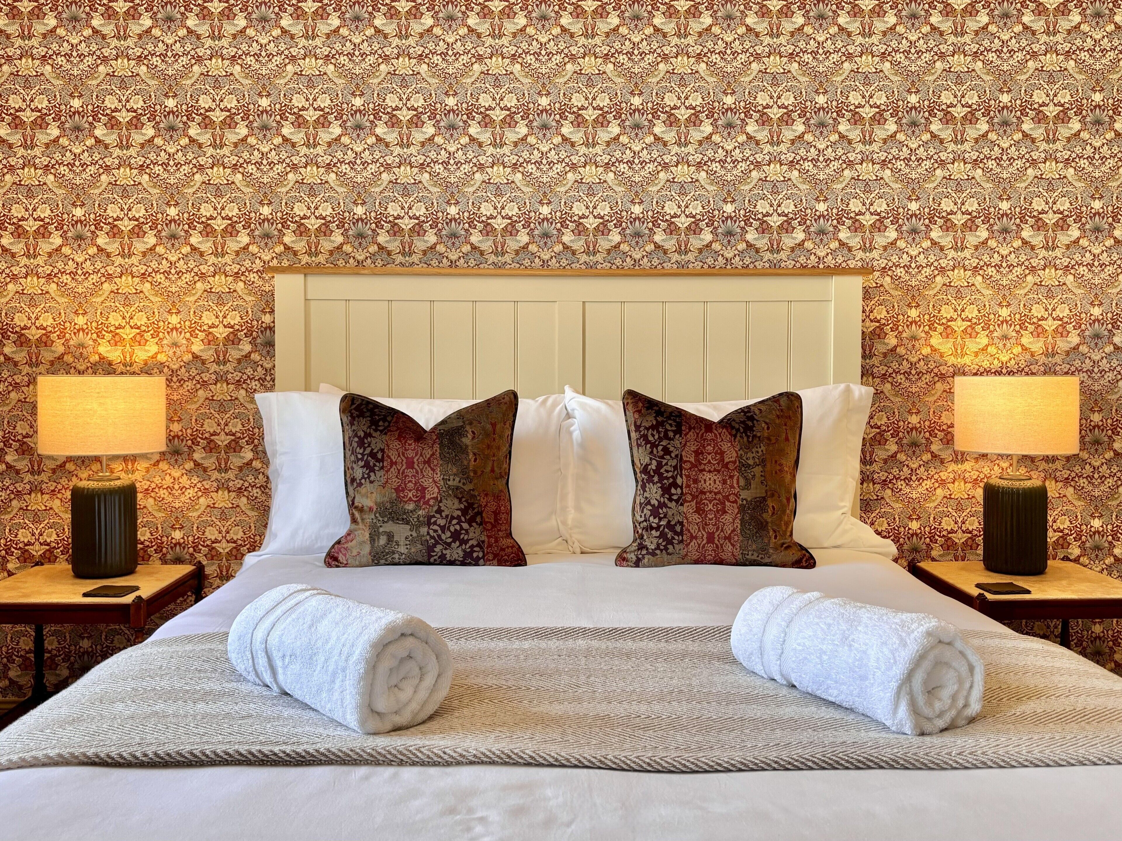 Een hotelkamer met een groot bed, twee nachtkastjes, twee lampen en behang met een patroon.