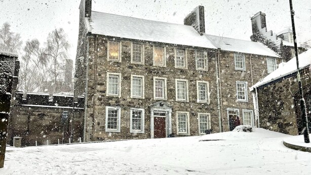 Un bâtiment en pierre doté de nombreuses fenêtres et dont le toit est recouvert de neige.