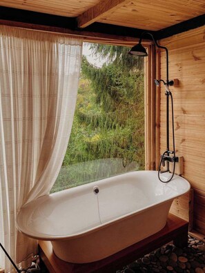 A wooden cabin with a large window, a bathtub, and a shower.