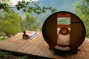 A wooden sauna with a large window, a wooden deck, and a person meditating on a mat.