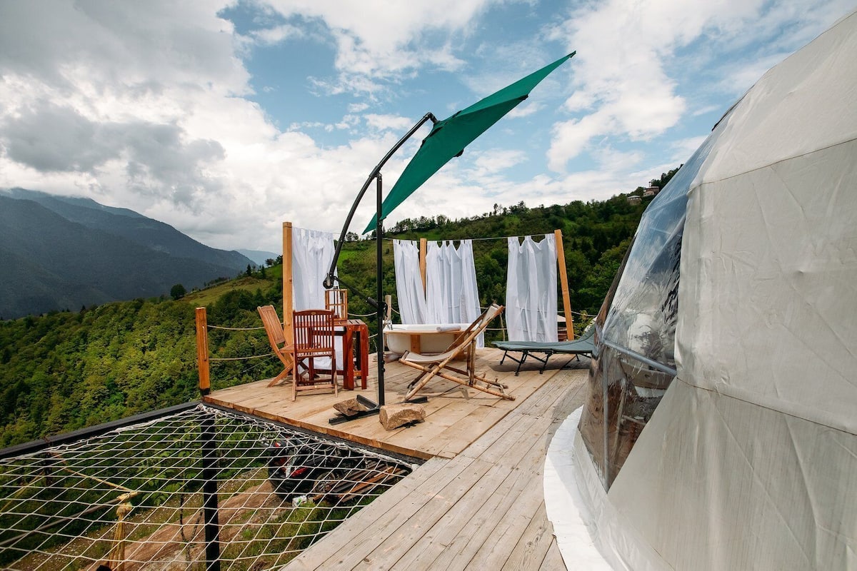 A wooden deck with outdoor furniture, a hot tub, and a view of a mountainous landscape.