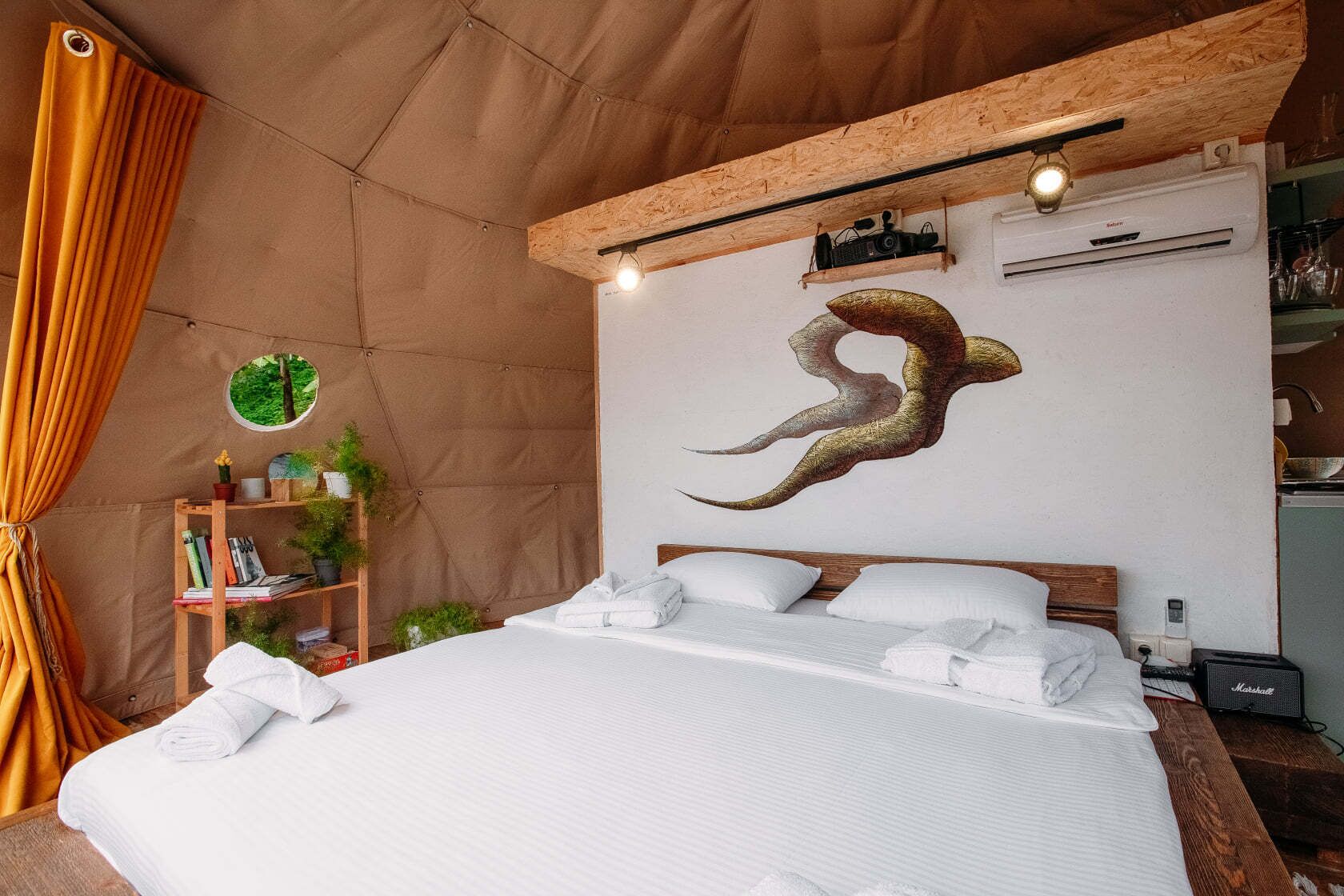 Habitación tipo tienda con una cama, una estantería, aire acondicionado de pared y una lámpara colgante.