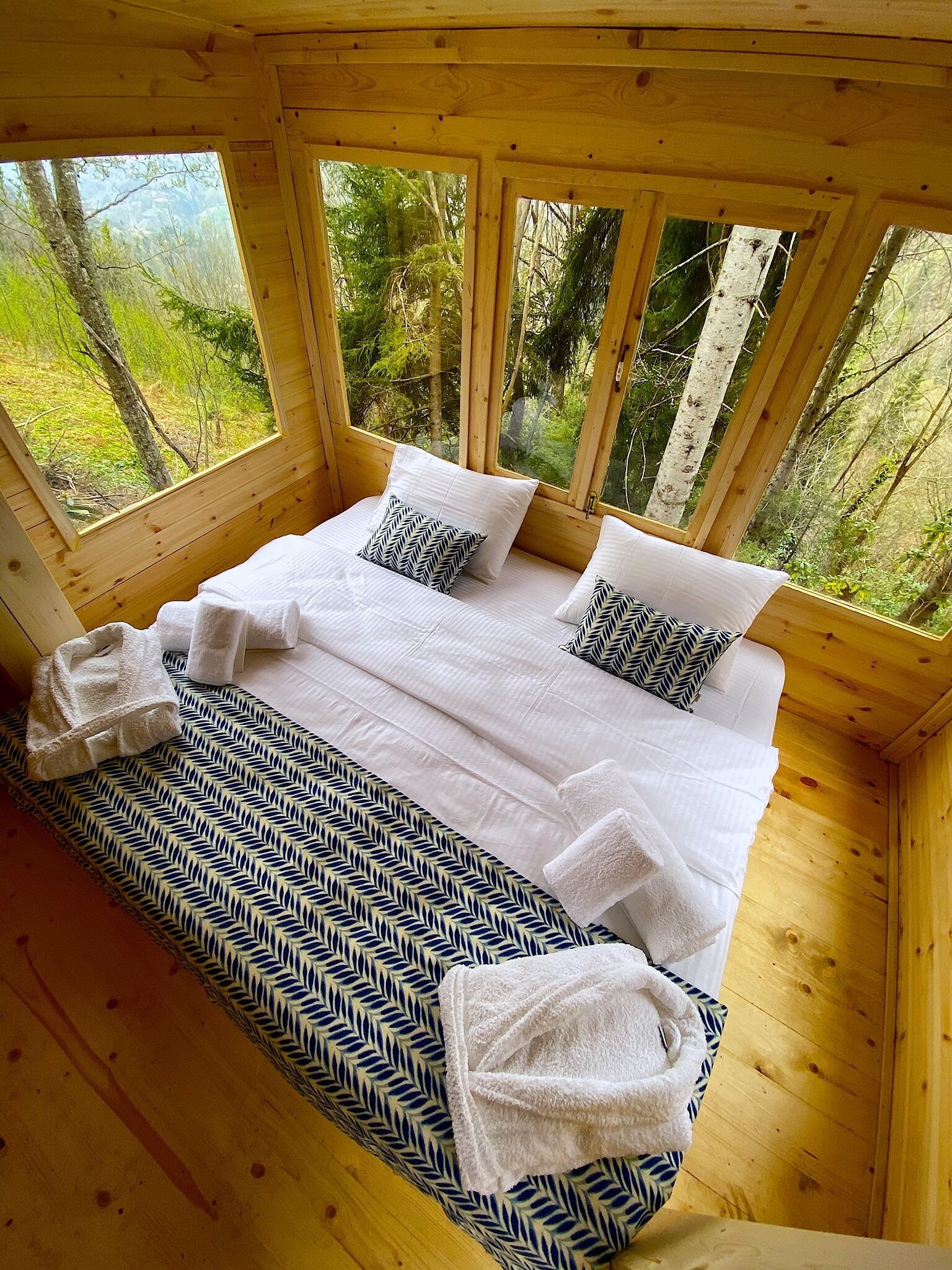 A wooden cabin bedroom with a bed, pillows, and a bench with towels.
