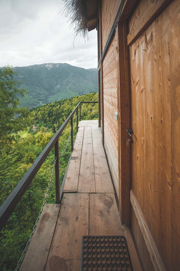 A wooden balcony with a metal railing overlooking a mountainous landscape.