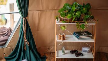 Una habitación acogedora con suelo de madera, cortina verde, estantería con libros y una planta, y una consola de videojuegos.