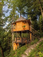 Una casa en árbol de madera con balcón y escaleras, rodeada por un bosque frondoso.