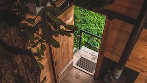 A wooden staircase leading to a door with a metal grate, surrounded by greenery. - Hill Inn (Keda)
