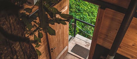 A wooden staircase leading to a door with a metal grate, surrounded by greenery.