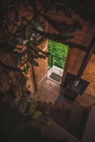Una escalera de madera que conduce a una puerta con celosía metálica, rodeada de follaje.