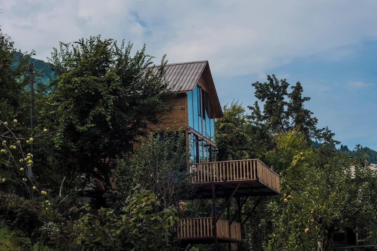 A treehouse with a wooden deck and a metal roof, surrounded by lush greenery.