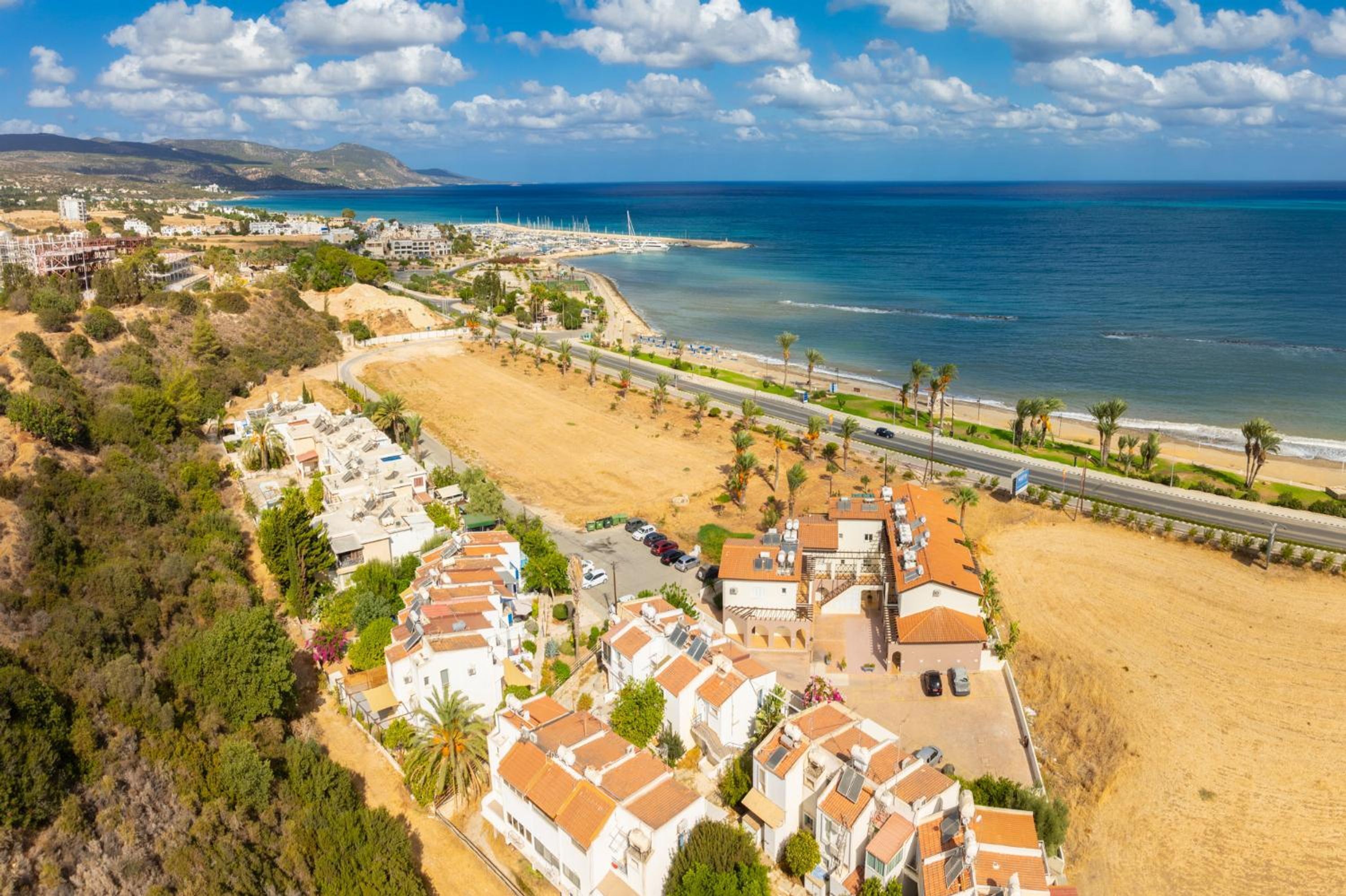 An aerial view of a coastal area with residential buildings, a beach, and a road leading to the sea.