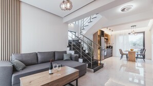 Een moderne woonkamer met een grijze bank, een houten salontafel en een trap naar een keukenruimte.