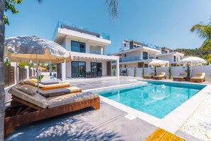 Een modern zwembadgedeelte met ligbedden en parasols, omringd door moderne gebouwen.