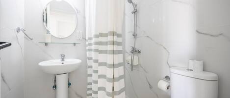 A bathroom with a white sink, mirror, shower, and toilet.