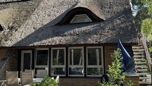 Ein rustikales Gebäude mit einem Strohdach, großen Fenstern und einer Steintreppe, die zum Eingang führt.