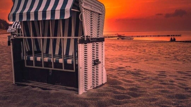 Ein Strandkorb mit gestreiftem Sonnendach an einem Sandstrand bei Sonnenuntergang.