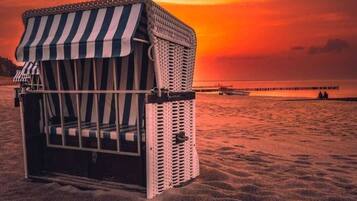 Ein Strandkorb mit gestreiftem Sonnendach an einem Sandstrand bei Sonnenuntergang.