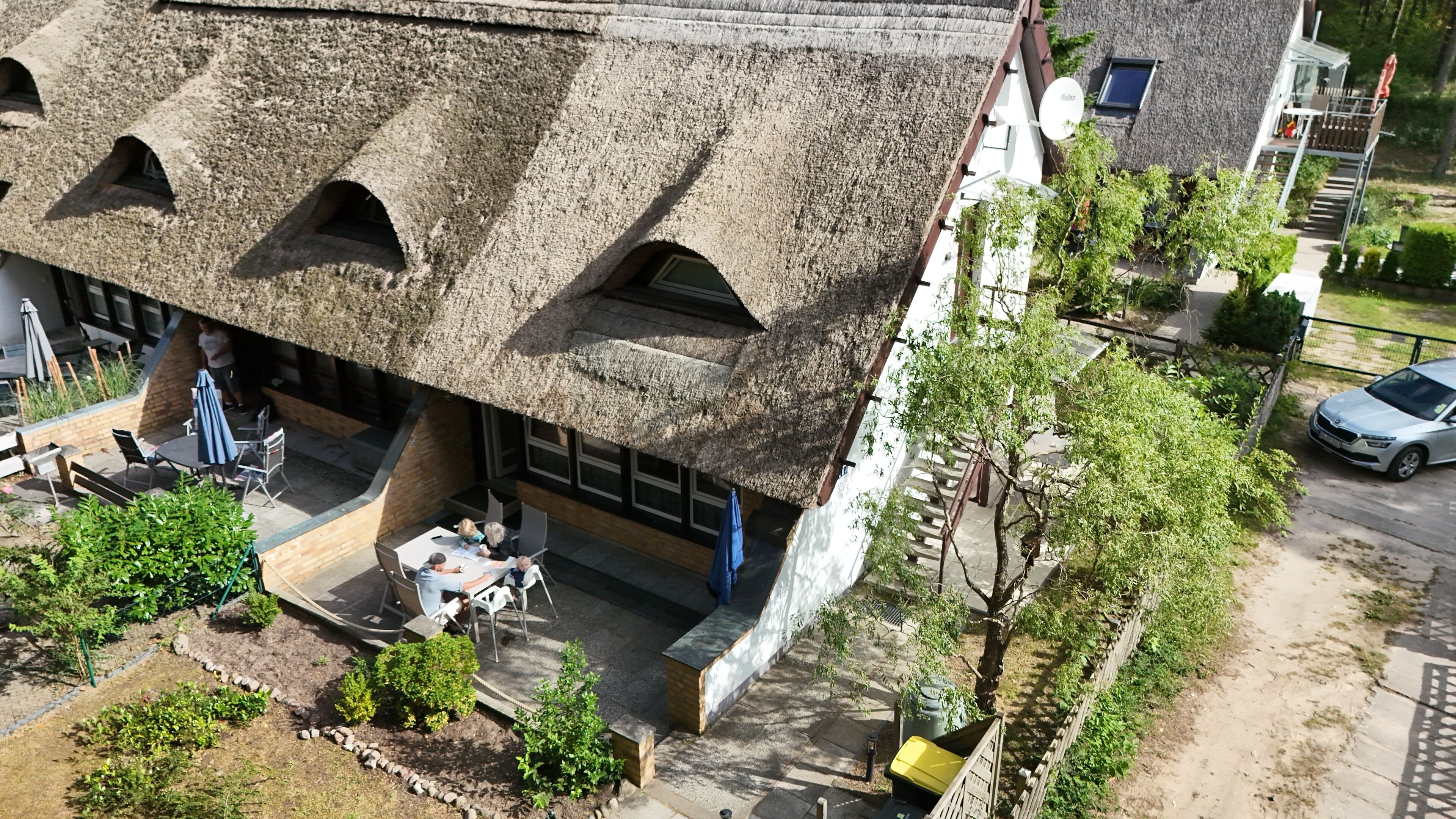 Ein Gebäude mit einem Strohdach, einem Außenbereich mit Sitzgelegenheiten und einer Treppe, die zu einer oberen Ebene führt.