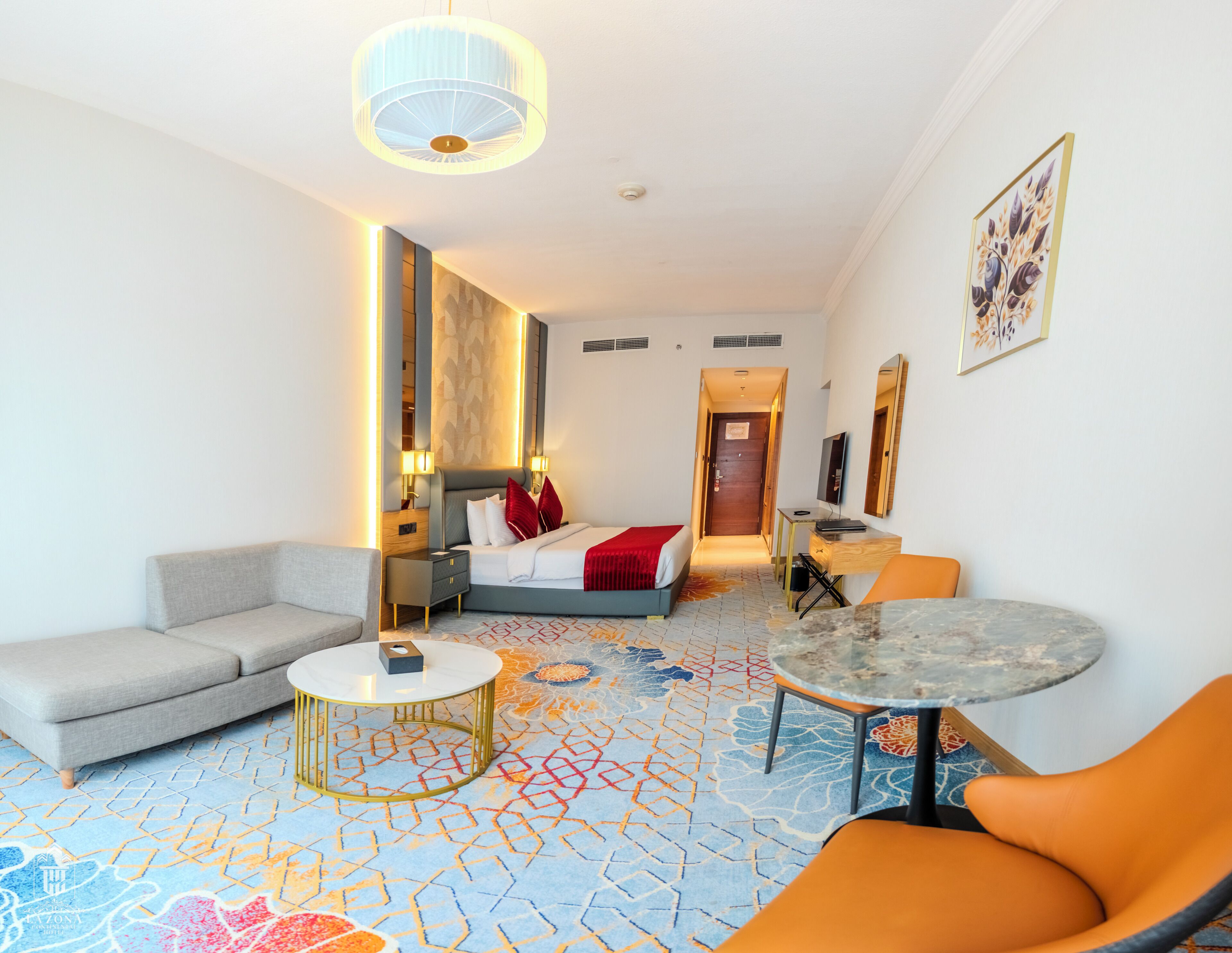A hotel room with a bed, a sofa, a small table, a chair, a desk, a television, and a patterned carpet.