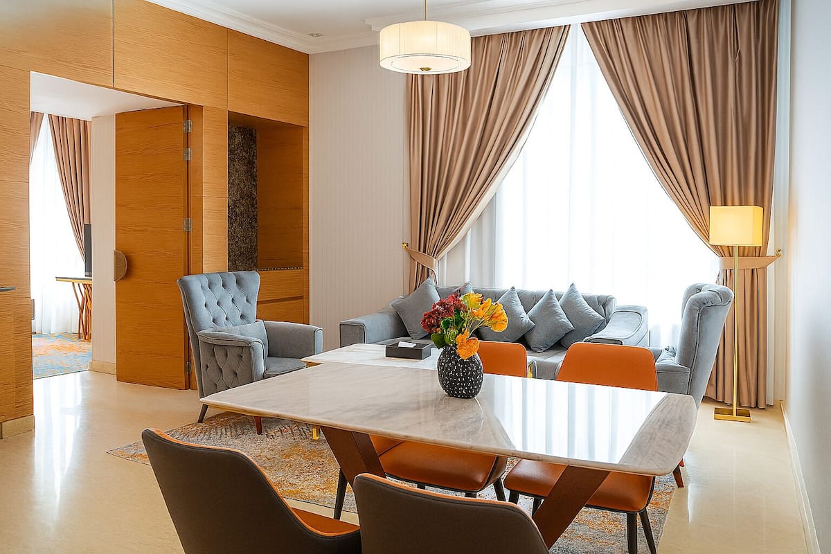 Un salon moderne comprenant une table à manger, des canapés et une grande fenêtre agrémentée de rideaux.