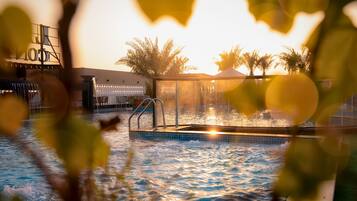 Un espace piscine doté d’un jacuzzi, entouré de palmiers et délimité par une clôture.