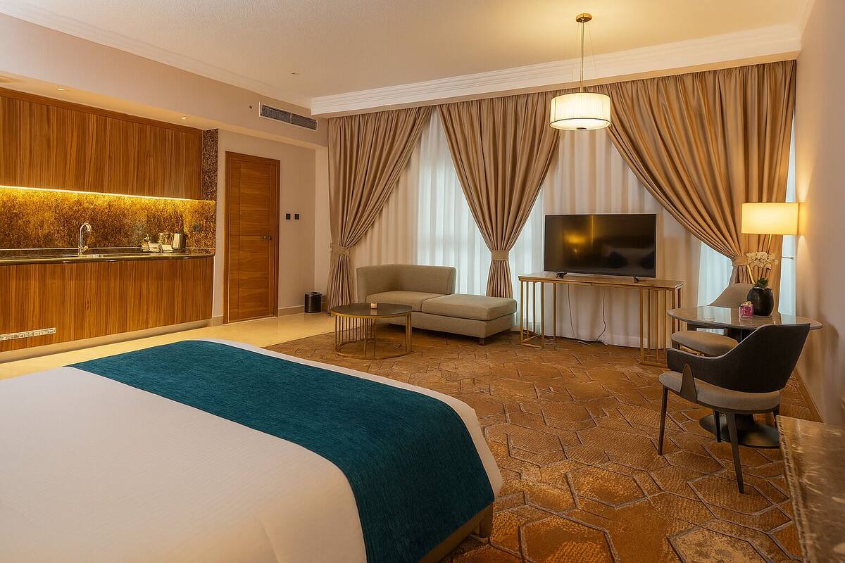 Une chambre d’hôtel dotée d’un grand lit, d’une télévision, d’un coin salon avec un canapé et des fauteuils, d’une petite table et d’un mini-bar.
