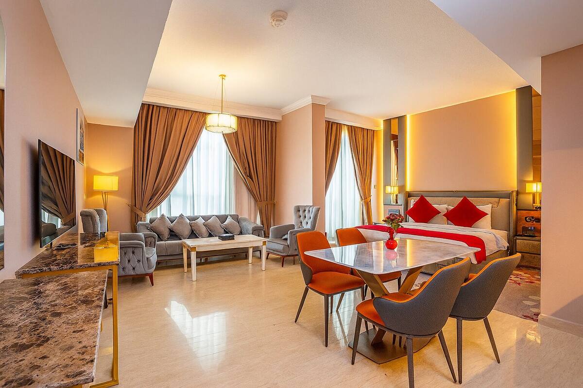 Une chambre d’hôtel comprenant un coin repas, un canapé, un lit avec des oreillers rouges et un grand miroir.