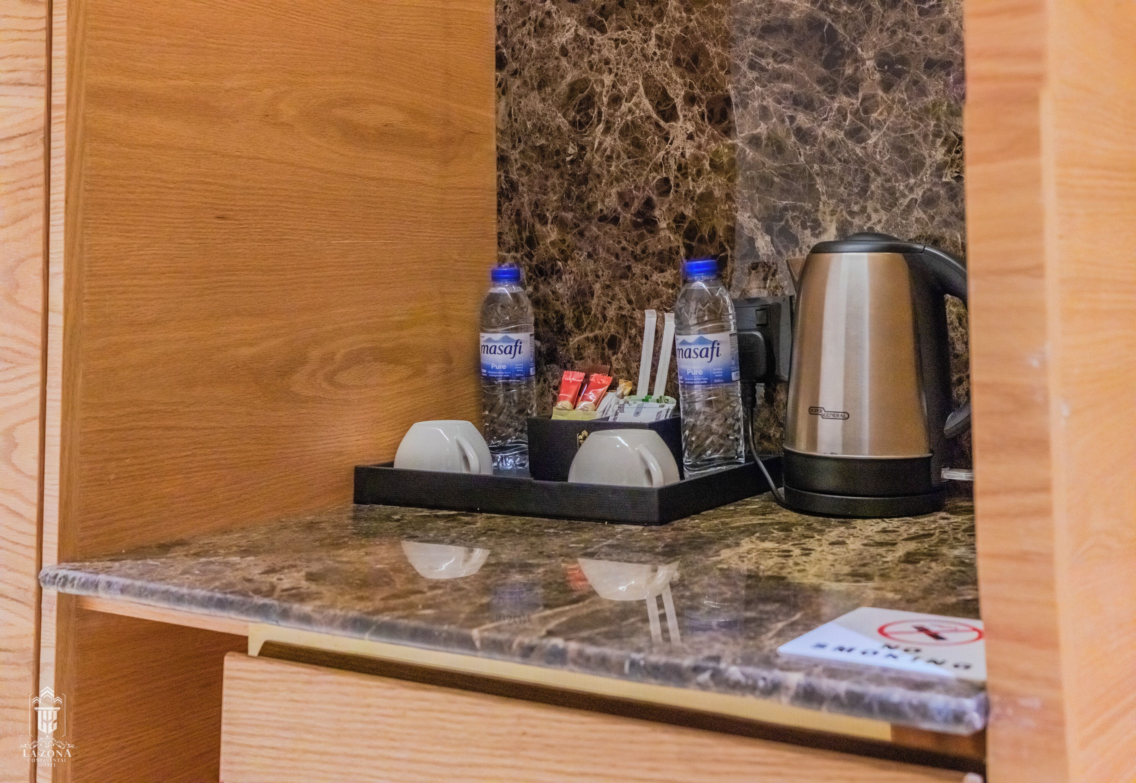 A hotel room's minibar with a coffee maker, two water bottles, and a glass of water.
