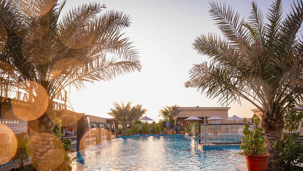 A swimming pool with palm trees, a waterfall feature, and a lifeguard stand. - La Zona Continental Hotel (Dubai)