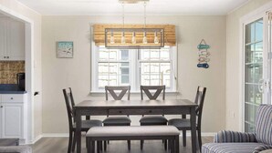 Un coin repas avec une table en bois et six chaises, un banc, un fauteuil à rayures et une fenêtre avec un store en bambou.