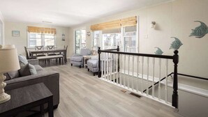 Un vaste espace de vie comprenant un canapé, des fauteuils et une table à manger. Un escalier doté d’une rampe mène à l’étage supérieur.
