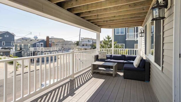 Une véranda couverte avec un plafond en bois, une balustrade blanche et un espace salon comprenant un canapé et une table.