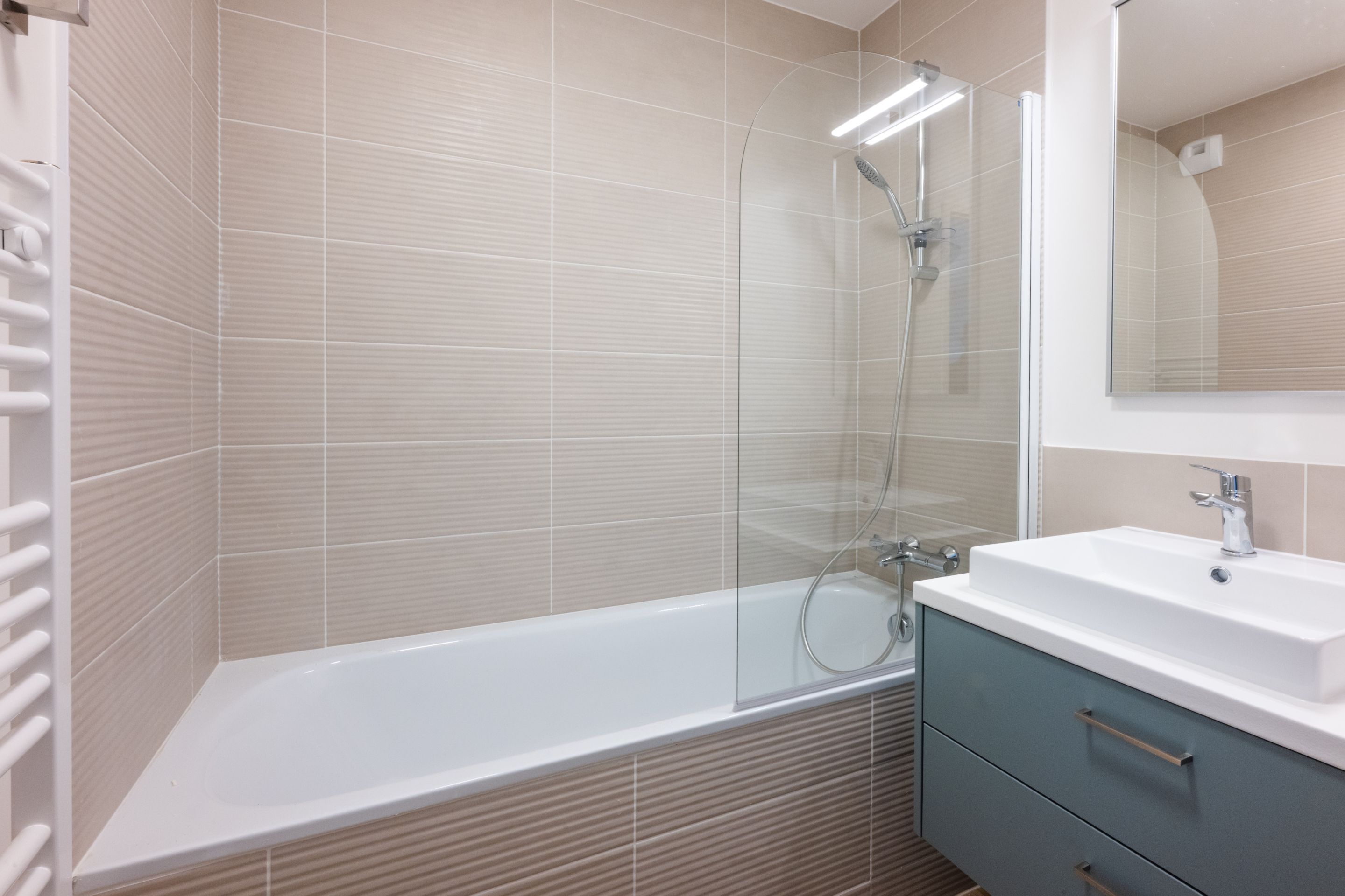 A modern bathroom with a glass-enclosed shower, a white bathtub, and a vanity with a mirror.