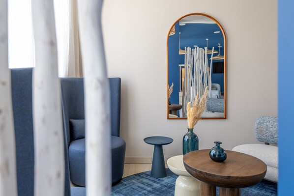 A modern living room with a blue sofa, a round wooden table, and a small blue side table. - Résidence Odalys Bleu Canopée (Mimizan)