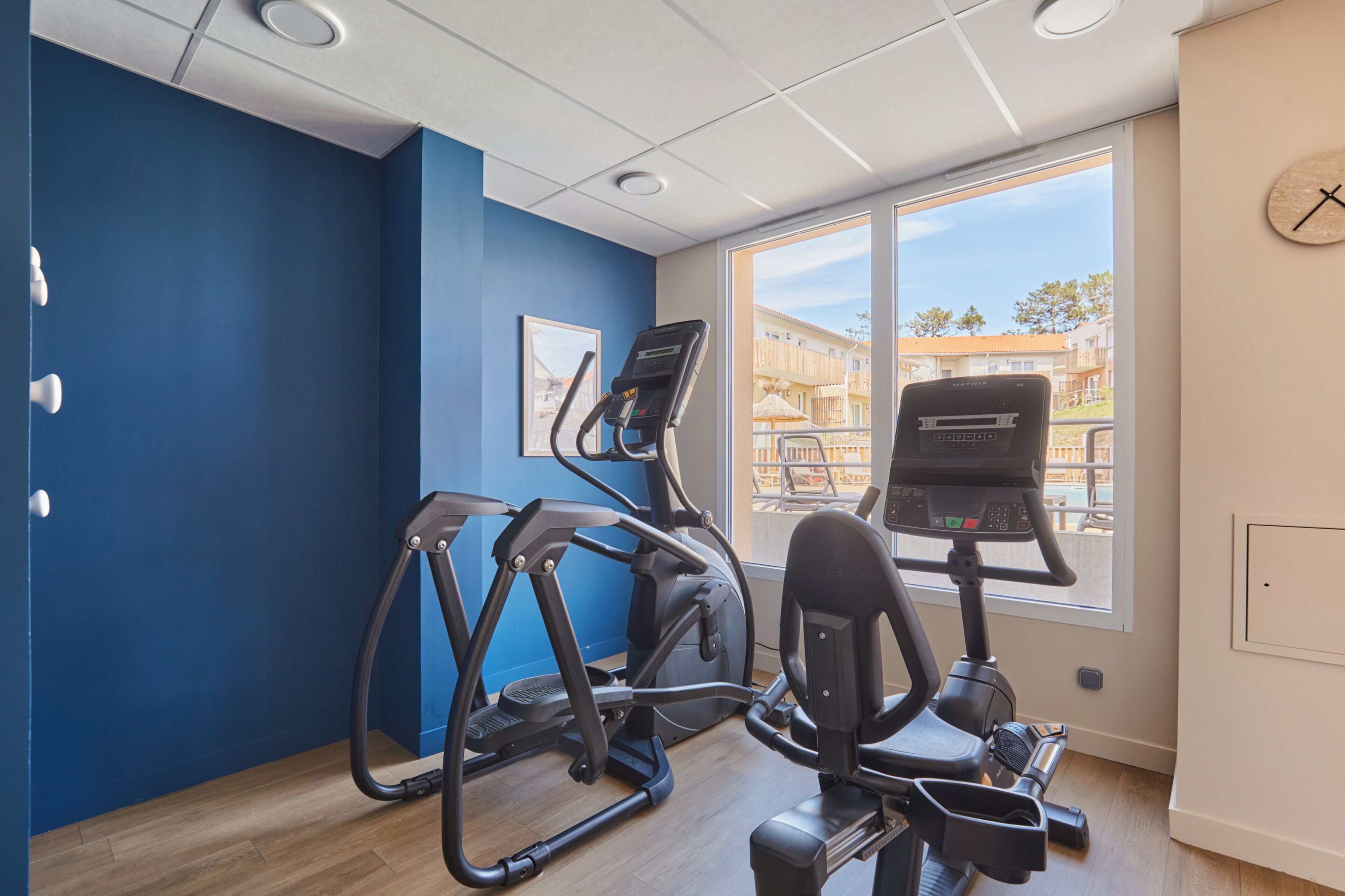 A gym with exercise equipment, a large window, and a clock on the wall.