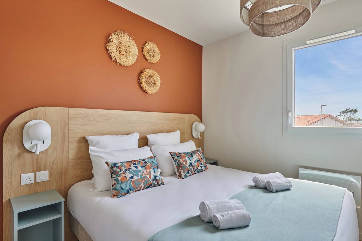 Hotelkamer met een houten hoofdeinde, wit beddengoed, decoratieve wandkunst, een bedlampje en uitzicht.
