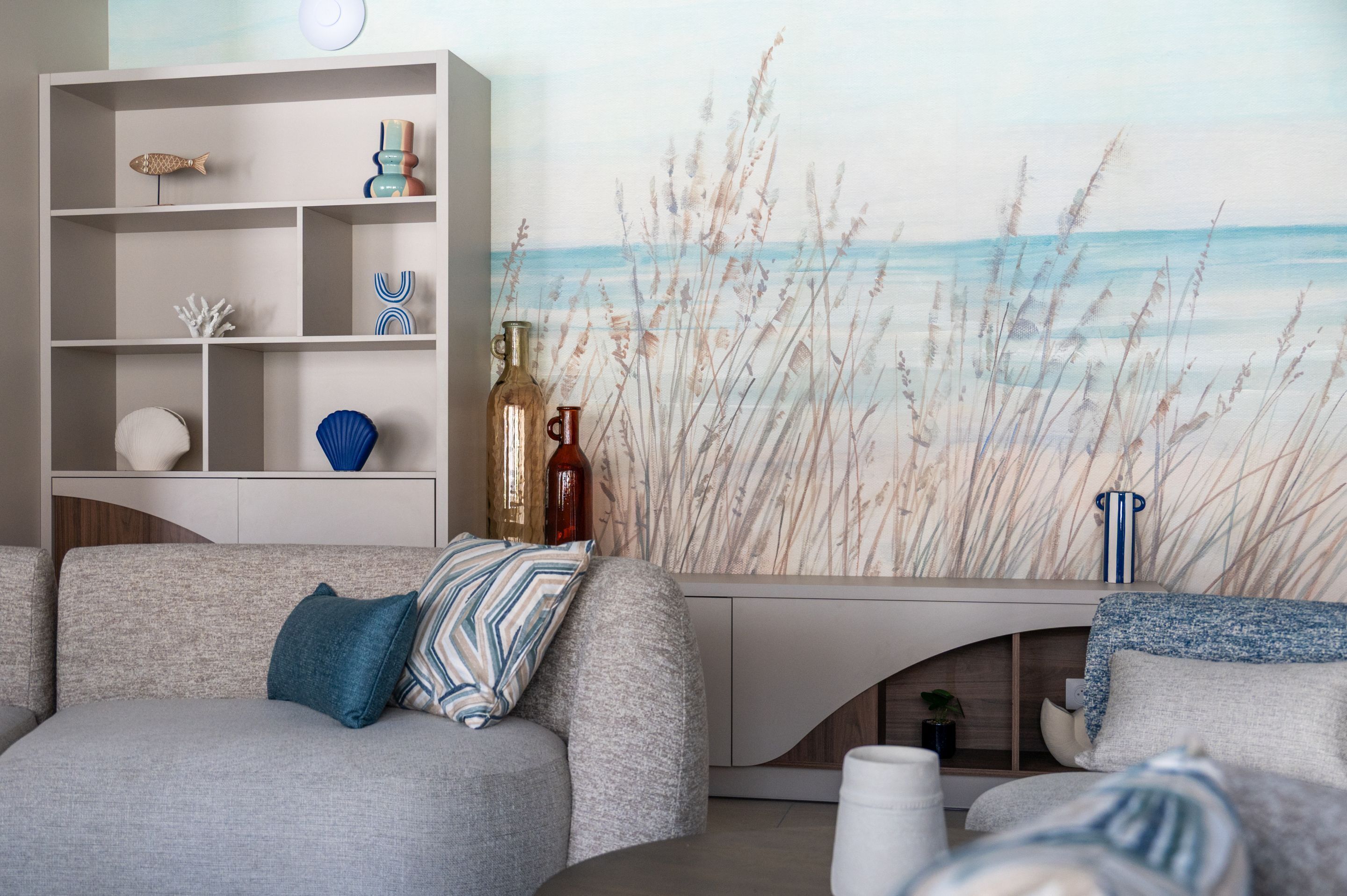 En moderne stue med en grå sofa, et hvidt konsolbord og et vægmaleri med strandtema.