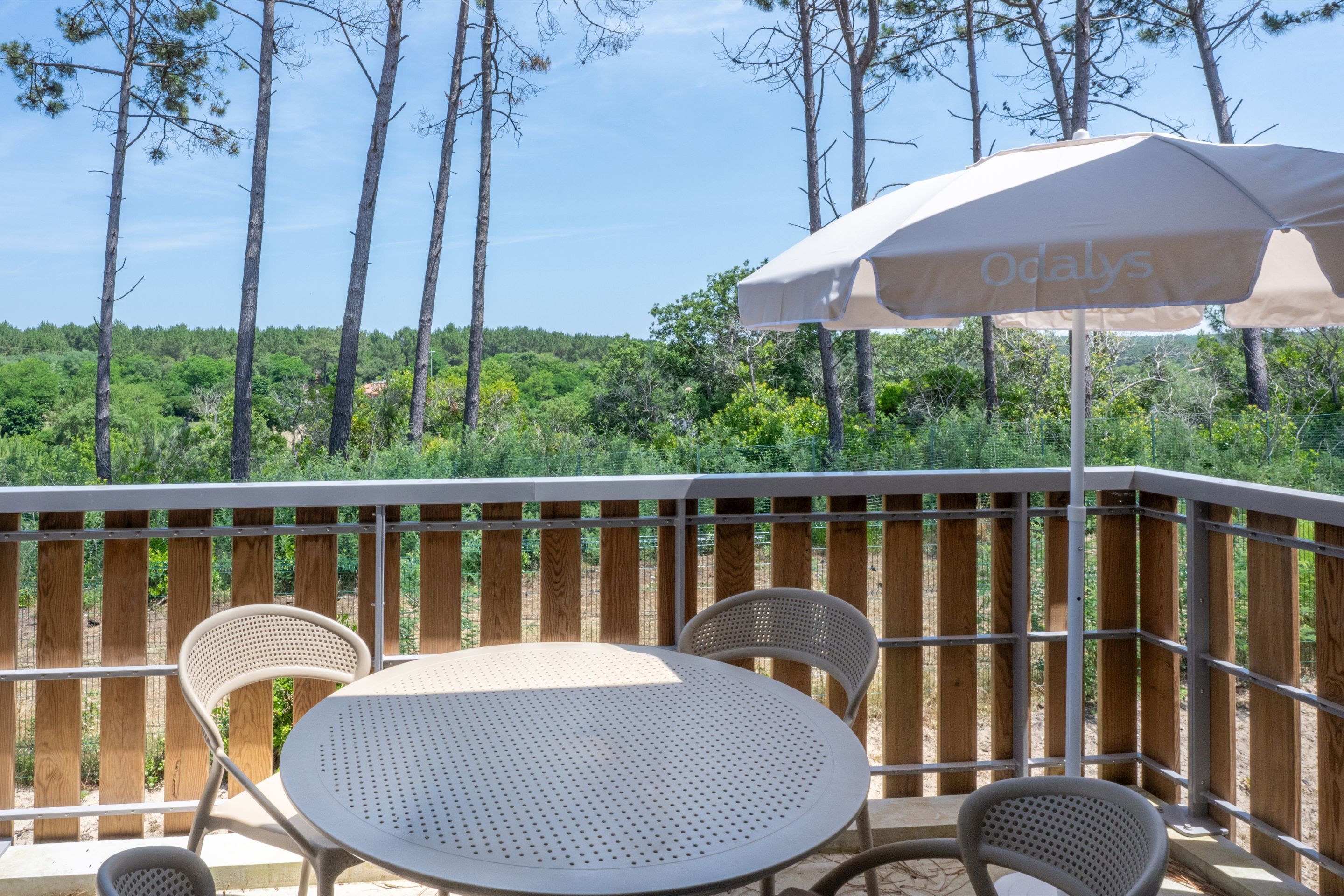 An outdoor patio with a round table and two chairs, an umbrella, and a wooden fence.