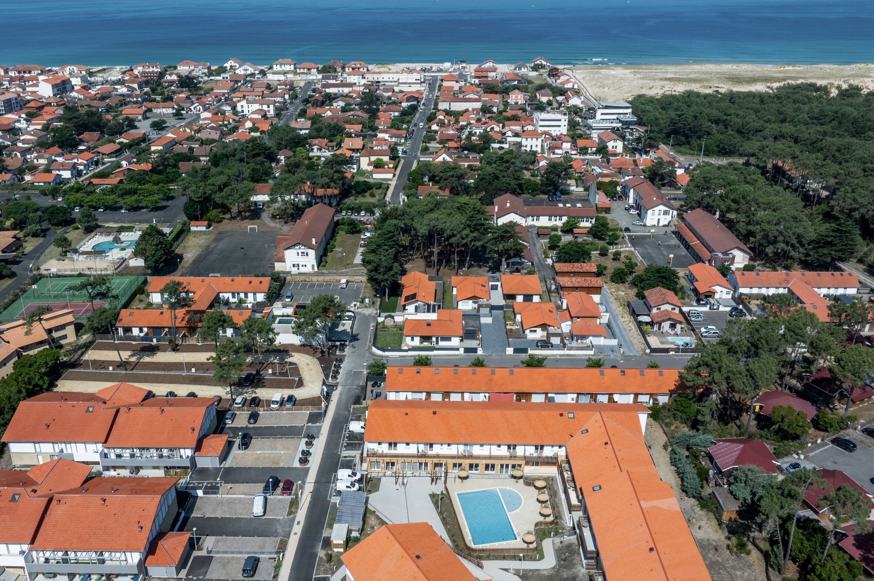 Ett flygbildsbild av ett bostadsområde vid kusten med hus, en strand och en swimmingpool.