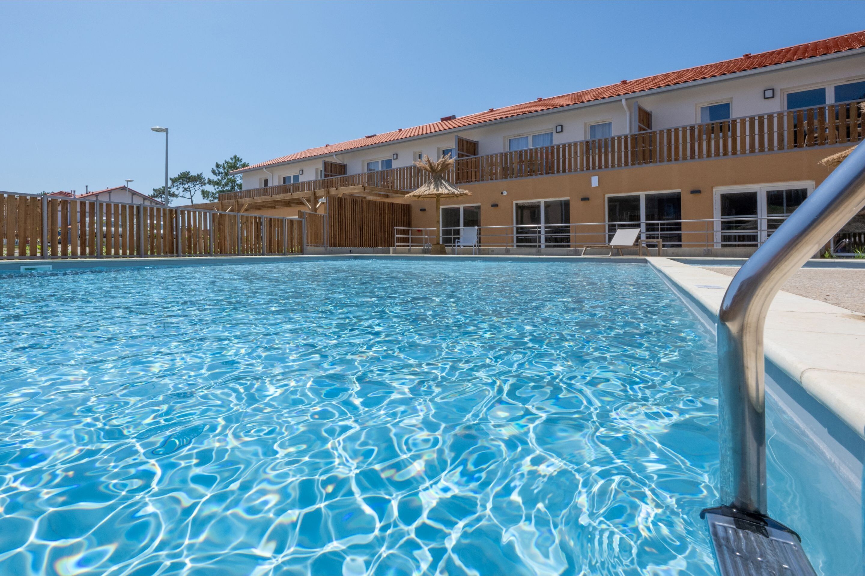 A swimming pool with clear water, a wooden fence, and a building with balconies in the background.