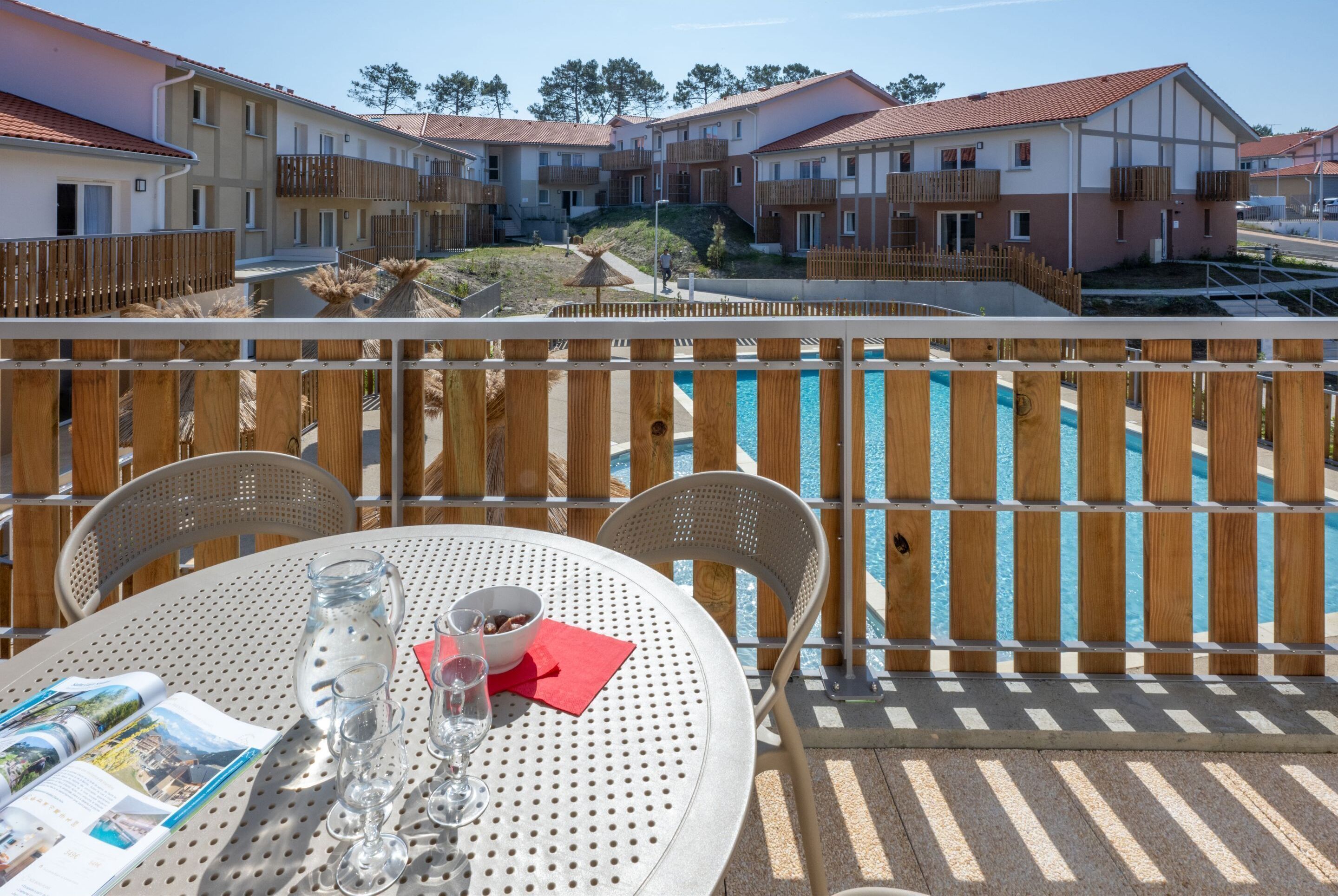 Una terraza con piscina, cerco de madera y una mesa con menú y vasos.