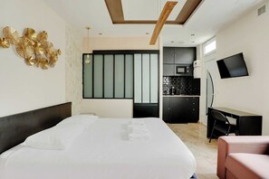 A modern hotel room with a large bed, a desk, a chair, a flat-screen TV, and a kitchenette. - Charming Studio - 2P - Montorgueil (Paris)
