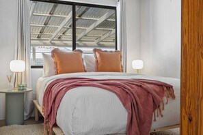 Une chambre à coucher avec un lit, des oreillers, des tables de chevet, une fenêtre et une vue sur le toit.
