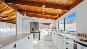Cozinha moderna com armários brancos, geladeira de aço inoxidável e teto de madeira.