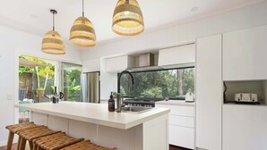 A modern kitchen with a central island, white cabinetry, and a view of greenery outside. - Bangalow Retreat in Buderim (Mooloolaba Region)