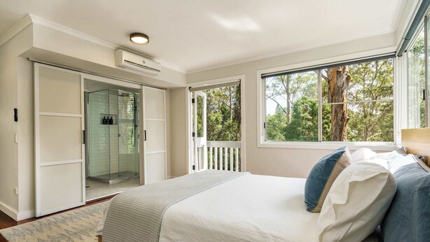 A bedroom with a bed, a walk-in closet, a glass shower, and a view of trees. - Bangalow Retreat in Buderim (Mooloolaba Region)
