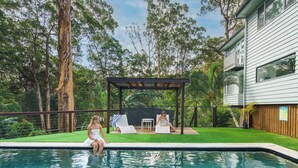 A swimming pool with two lounge chairs, a pergola, and a house in the background. - Bangalow Retreat in Buderim (Mooloolaba Region)