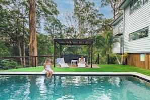 Une piscine avec deux chaises longues, une pergola et une maison en arrière-plan.